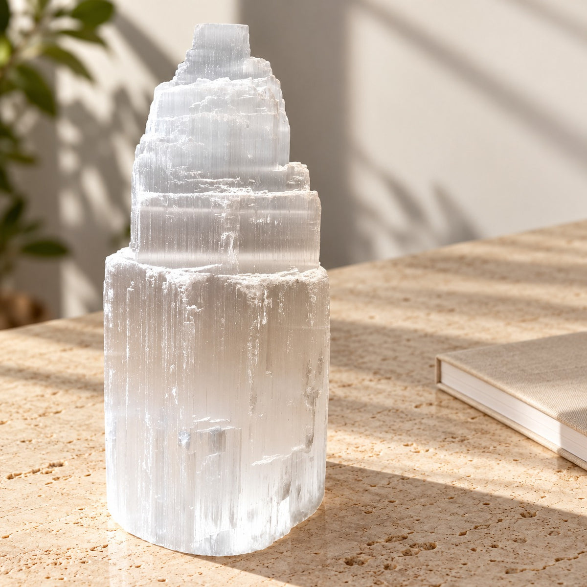 Tour en sélénite blanche à étages, posée sur une table en pierre claire.