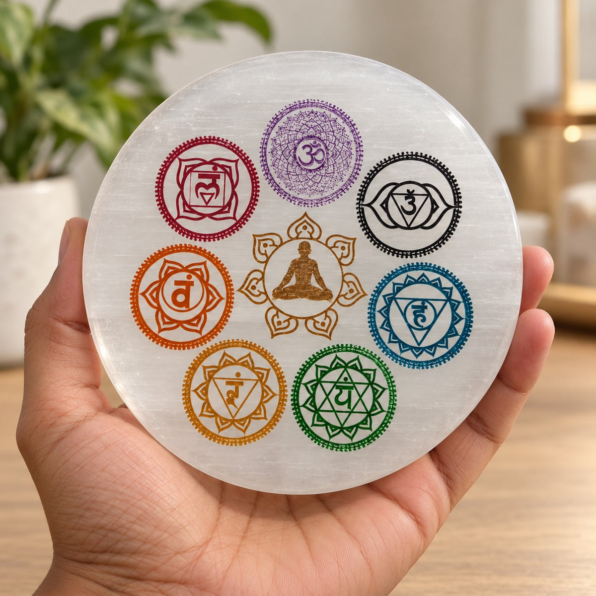Disque en sélénite orné des sept symboles colorés des chakras, tenu dans une main. 