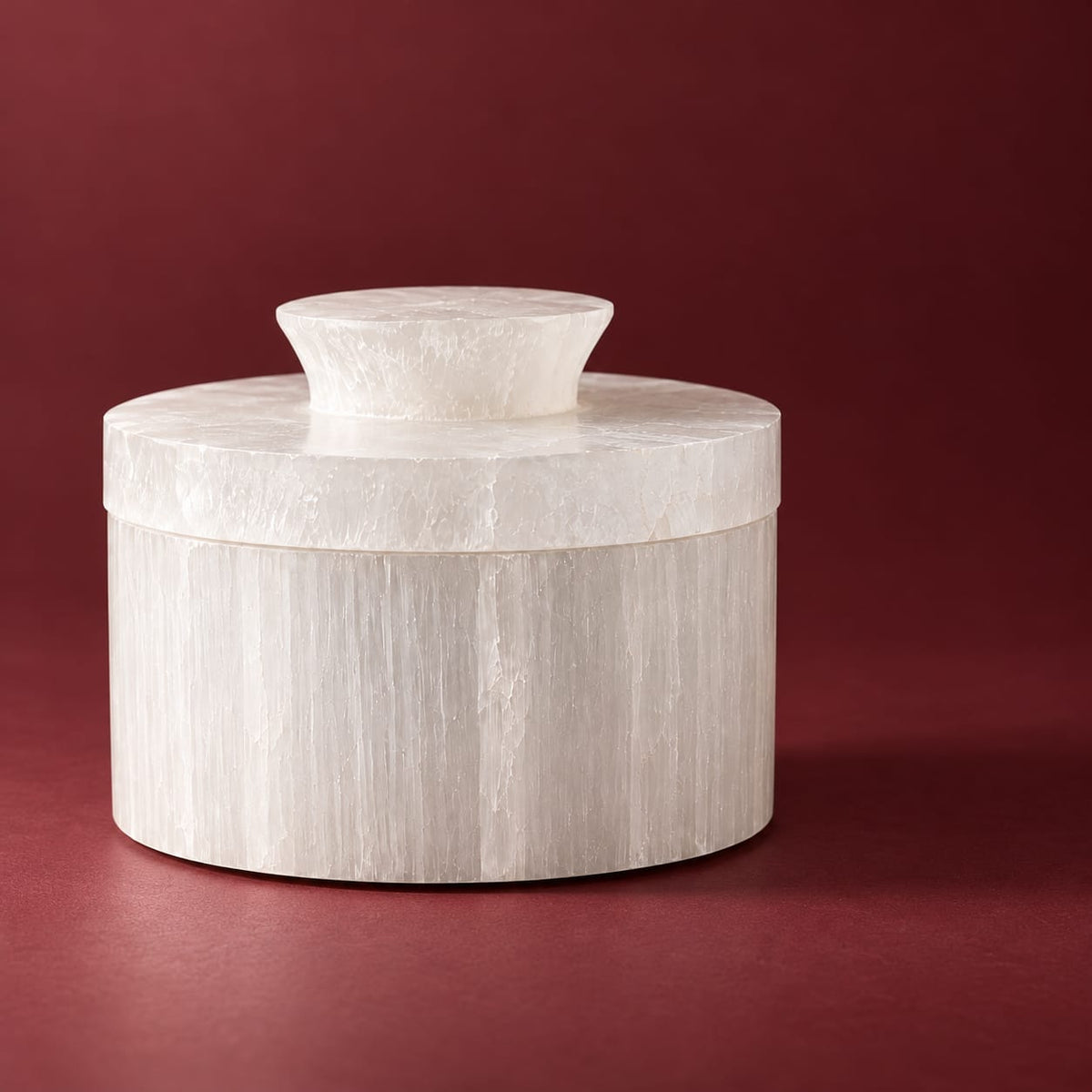 Boîte cylindrique en sélénite fermée sur fond bordeaux — écrin spirituel artisanal fait main au Maroc, cadeau bien-être unique | Pure Selenite