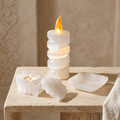 Coffret Lumière Sacrée en sélénite : lampe bougie allumée, bougeoir avec son couvercle et bol carré sur une table en pierre claire.